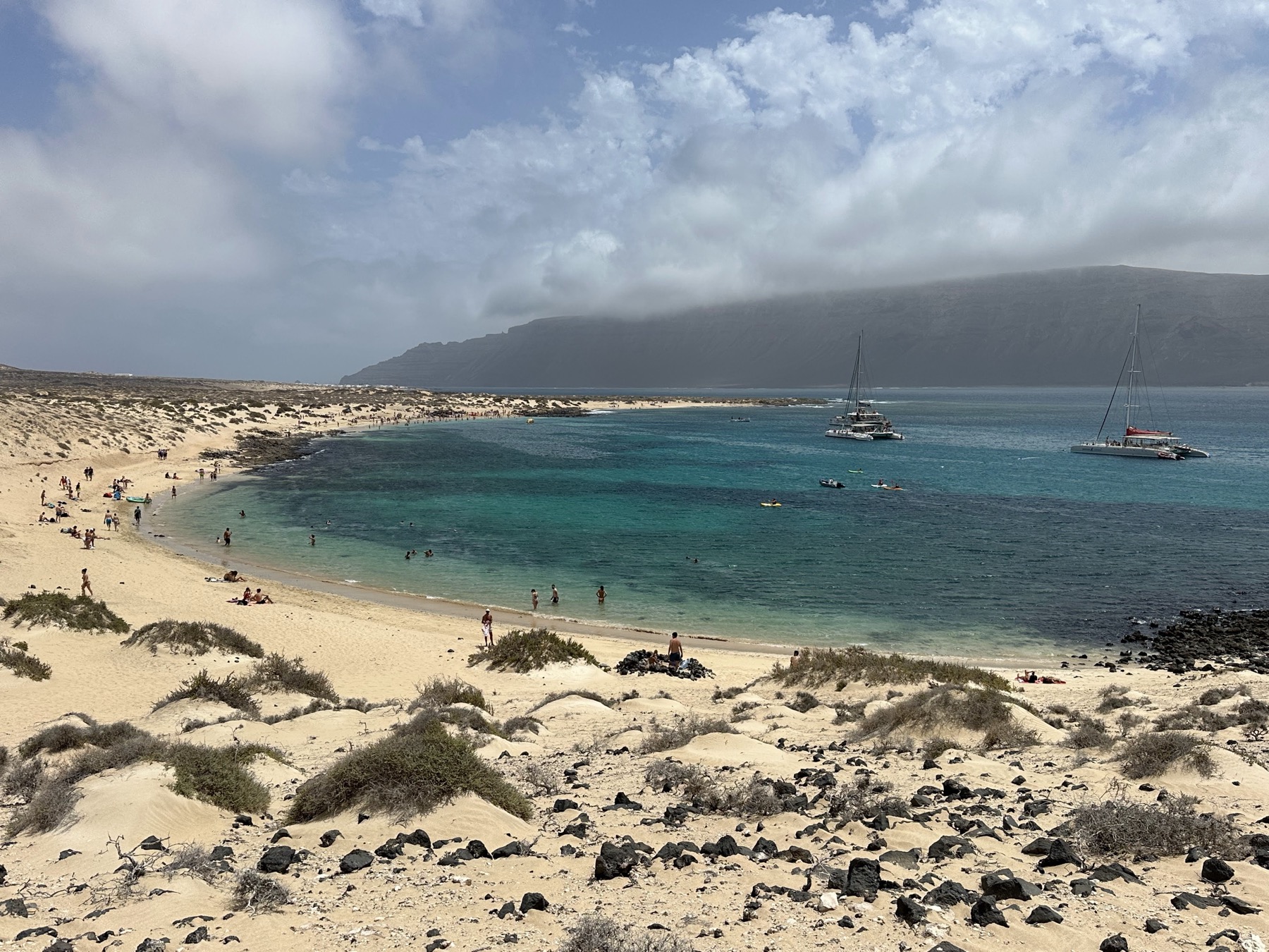 Playa de arena clara y mar turquesa en La Graciosa con barcos y montañas al fondo
